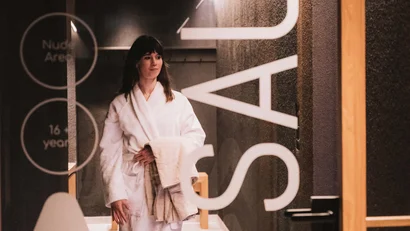 Frau im Bademantel läuft im Spa-Flur mit Handtüchern in der Hand