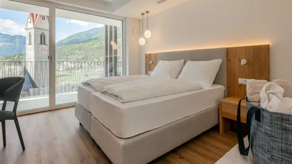 Modern hotel room with double bed and view of church tower and mountains