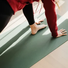 Person in einer Yoga-Dehnung auf einer grünen Matte im Sonnenlicht
