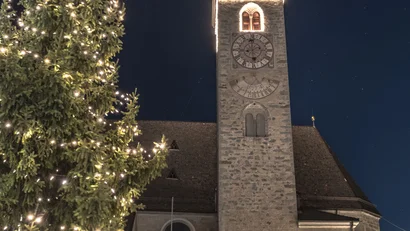 Beleuchteter Weihnachtsbaum vor einem steinernen Kirchturm bei Nacht