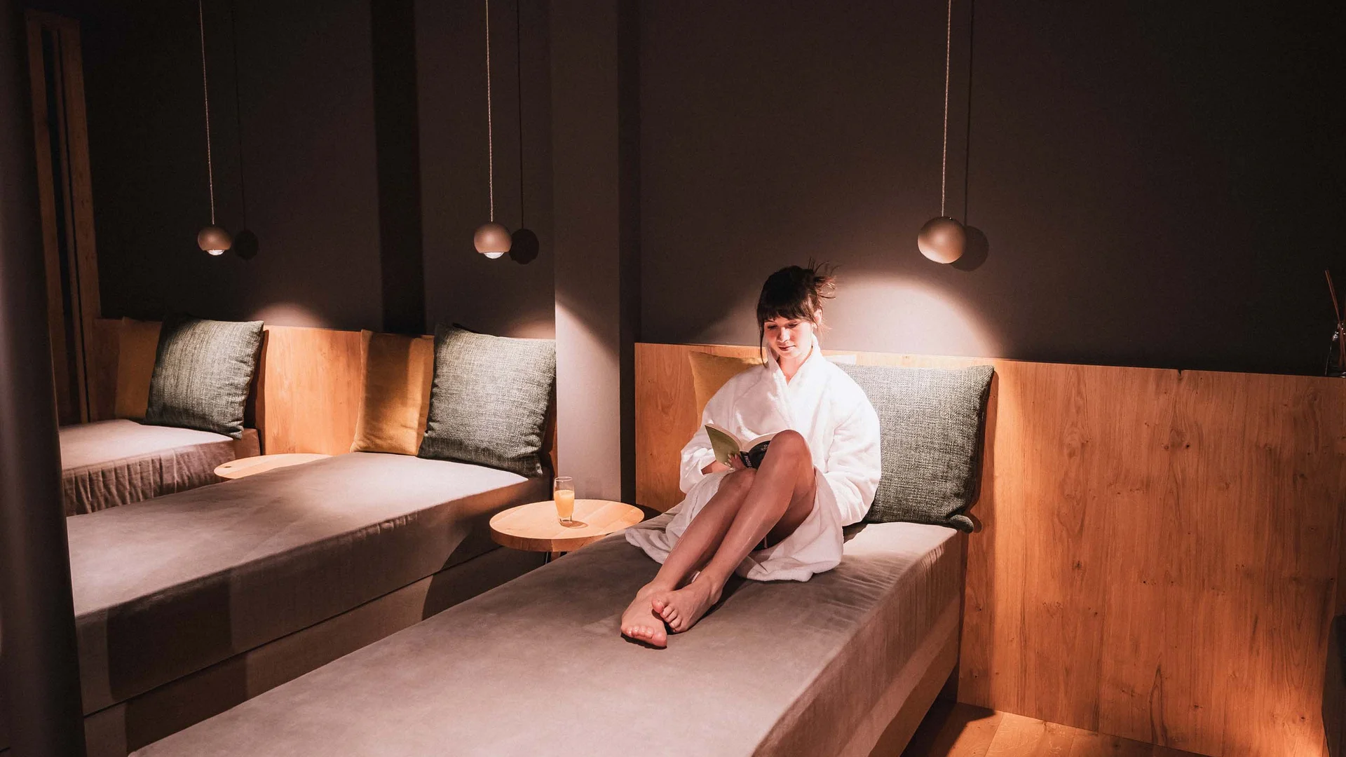 Frau in Bademantel liest entspannt auf Liege in gemütlichem Raum