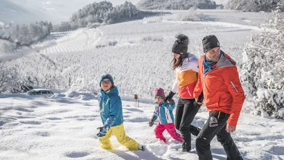 Familie wandert durch eine verschneite Landschaft mit bewaldeten Hügeln