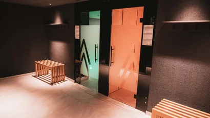 Dunkler Spa-Raum mit Holzbänken und zwei farbigen Saunatüren