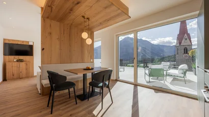 Living area with wooden furniture and terrace overlooking mountains and church tower