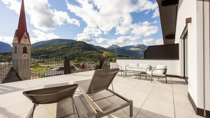 Terrace with loungers and seating area overlooking mountains and church tower
