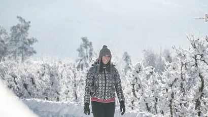 Frau geht auf einem verschneiten Weg zwischen frostbedeckten Bäumen