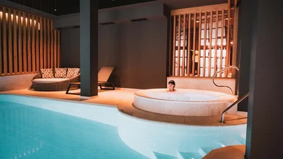 Person entspannt im Whirlpool neben einem beleuchteten Pool in modernem Innenraum