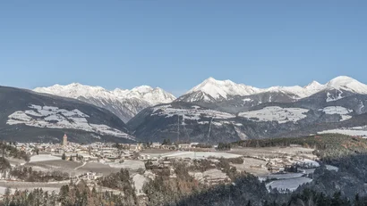 Verschneites Dorf in einem Tal vor einer Reihe schneebedeckter Alpenberge