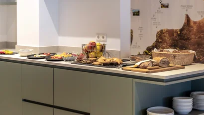 Buffet with fruit, pastries, bread, and plates on a kitchen counter