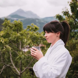 Frau im Bademantel genießt Getränk vor Bergkulisse