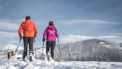 Zwei Wanderer mit Stöcken unterwegs durch eine verschneite Berglandschaft