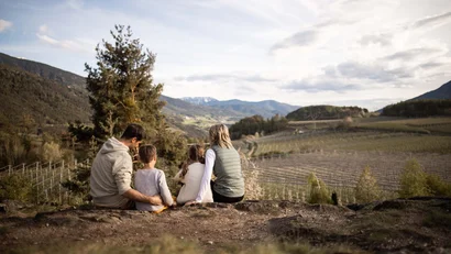 Familie sitzt auf Felsen und blickt auf ein Tal mit Weinbergen
