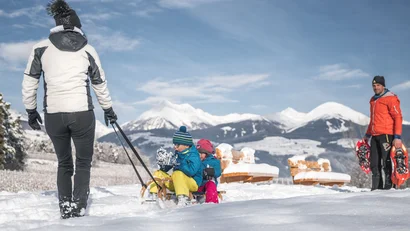 Eine Frau zieht zwei Kinder auf einem Schlitten durch eine verschneite Berglandschaft