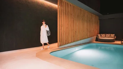 Frau im Bademantel geht an einem hell erleuchteten Innenpool entlang