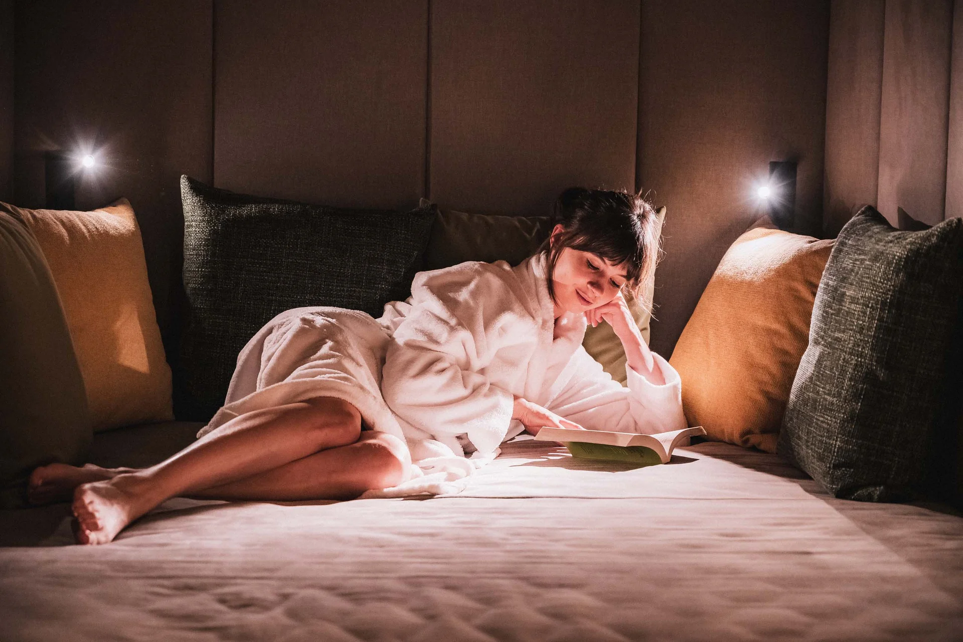 Ferienwohnung in Natz-Schabs – Aparthotel mit Frühstück & Spa Frau in weißem Bademantel liest entspannt auf einem großen Bett mit Kissen