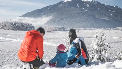 Drei Personen sitzen im Schnee vor einer verschneiten Berglandschaft