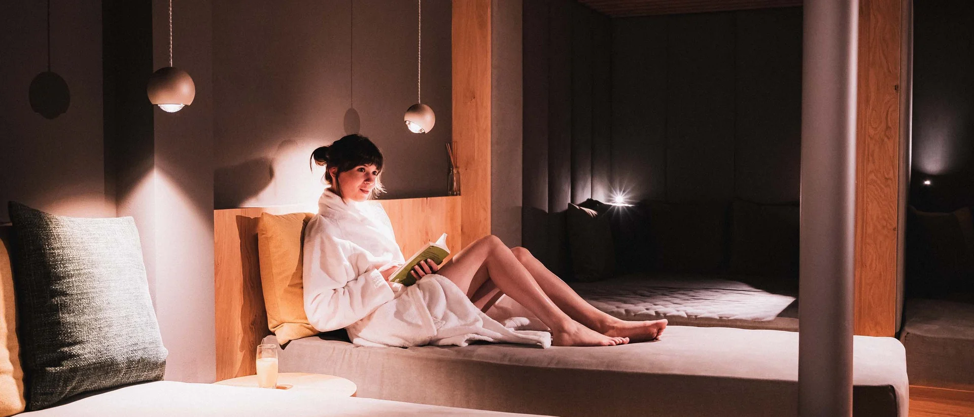 Ferienwohnung in Natz-Schabs – Aparthotel mit Frühstück & Spa Frau in Bademantel liest entspannt in modernem, gedämpft beleuchtetem Zimmer