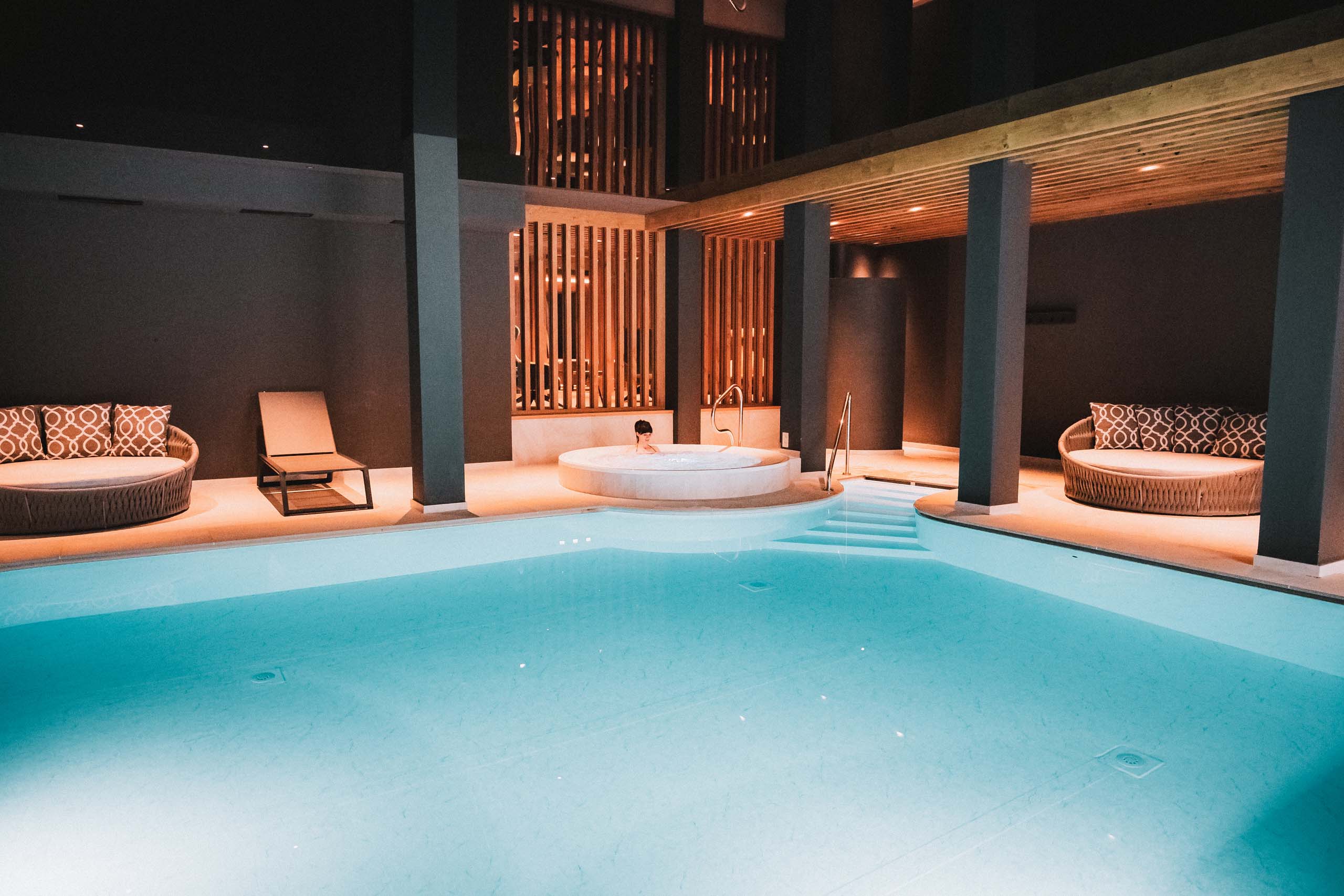 In einem modernen Innenpool mit Whirlpool sitzt eine Person entspannt im Wasser.